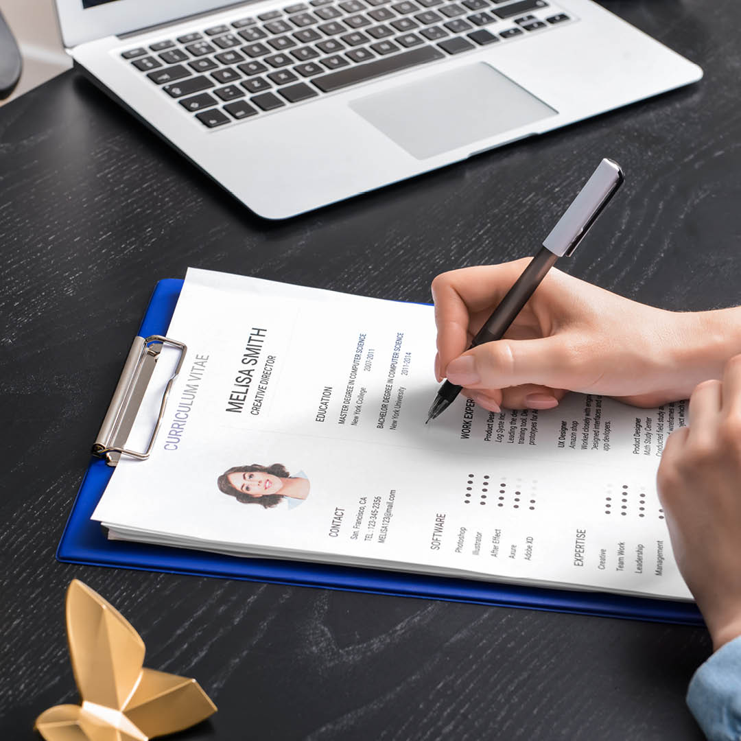 Fotografia delle mani di una persona con un evidenziatore in mano che scorrono un curriculum vitae appoggiato su una scrivania