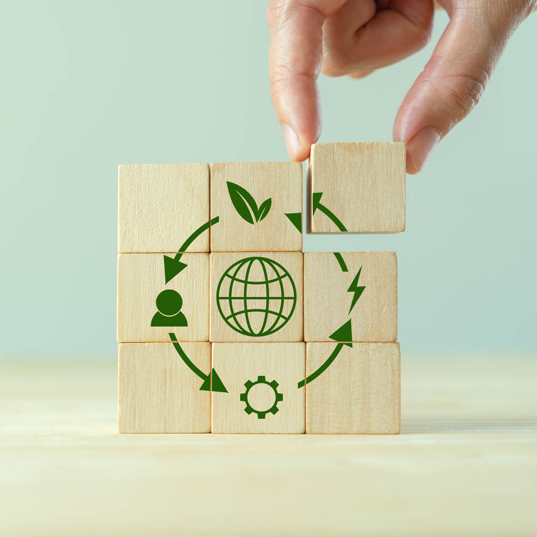 Fotografia di una mano che tiene un pezzo di un puzzle di legno decorato con simboli ecologici e un'icona del mondo in verde.