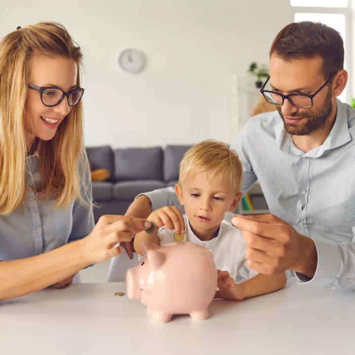 una madre, con il bambino ed il papà che inseriscono monetine nel salvadanaio a forma di maialino