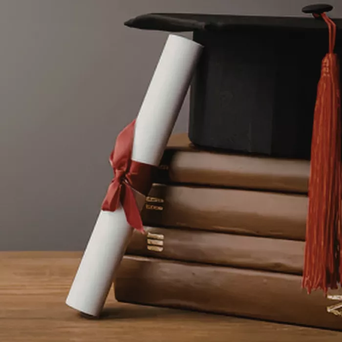 Una pergamena di laurea appoggiata ad alcuni libri ed al tocco di laurea