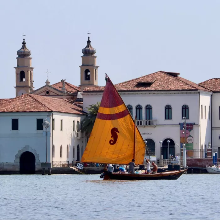 barca con vela arancione davanti all'isola di San Servolo a Venezia