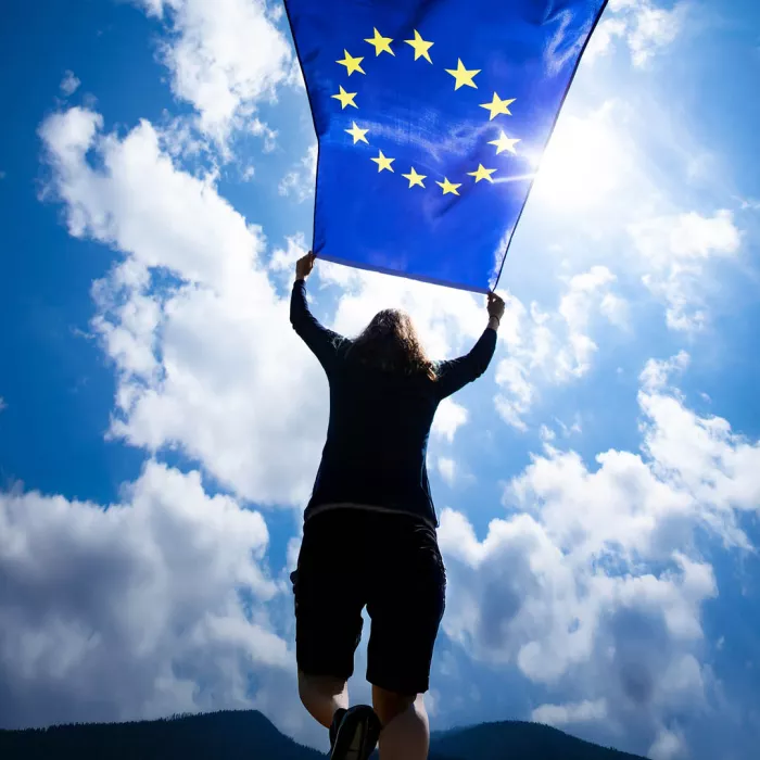 Giovane che salta e tiene bandiera Europea, in sfondo il cielo con nuvole
